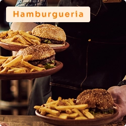 Garçom servindo pratos com hambúrgueres e batatas fritas em ambiente de hamburgueria, com foco na apresentação dos lanches.