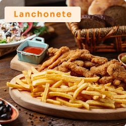 Tábua com porção de frango empanado e batata frita, acompanhada de molho vermelho, sobre mesa de lanchonete com outros pratos.